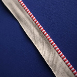 May include: A white fabric ribbon with red stripes against a dark blue background.