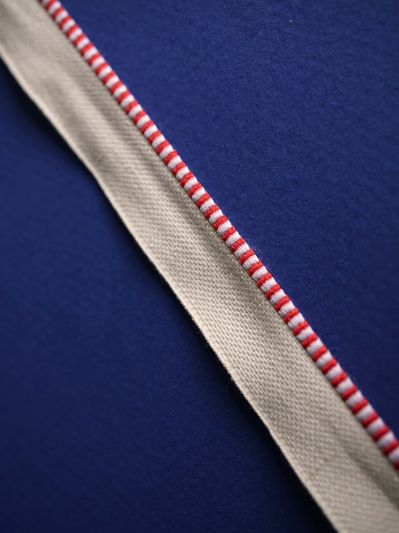May include: A white fabric ribbon with red stripes against a dark blue background.