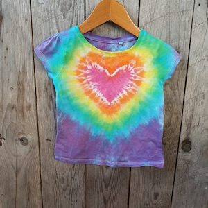 May include: A tie-dye t-shirt with a rainbow heart design. The shirt is purple, blue, green, yellow, and orange.