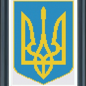 May include: Framed cross-stitch of the Ukrainian coat of arms, a gold trident on a blue background. The artwork is framed in a dark gray frame with a white matting. The cross-stitch design is detailed and precise.