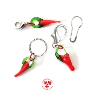 Puede incluir: Tres marcadores de punto de vidrio rojo y verde en forma de chile con un cierre de langosta plateado y un alfiler de seguridad plateado.