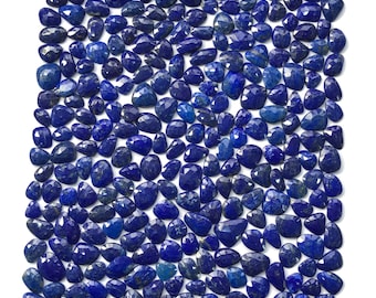 Puede incluir: Una colección de gemas de lapislázuli azul profundo facetadas. Las gemas varían en forma y tamaño, con una superficie pulida y reflectante. La disposición es densa, cubriendo todo el marco sobre un fondo blanco. Las piedras son de un azul rico y saturado.