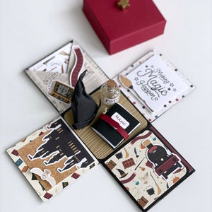 May include: A Harry Potter themed explosion box with a red box lid, a black hat, a potion bottle, a small notebook, and a card that says "Making Magic Happen".