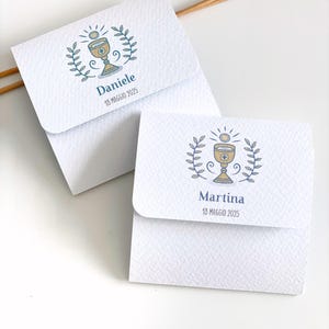 Könnte beinhalten: Zwei weiße Umschläge mit einem goldenen Kelch und einem Sonnenmotiv. Der obere Umschlag trägt die Aufschrift "Daniele 16 Maggio 2025" und der untere Umschlag die Aufschrift "Martina 18 Maggio 2025".