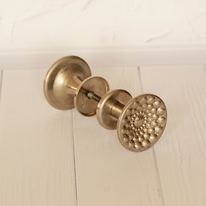 Può includere: Una maniglia per porta dorata con un design rotondo e testurizzato. La maniglia ha uno stile semplice ed elegante.