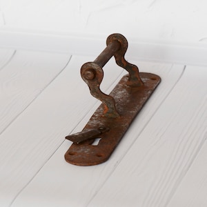 Peut inclure: Une poignée de porte en métal rouillé avec un levier et un trou de serrure. La poignée est fixée à une plaque métallique avec plusieurs vis.