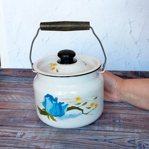 May include: White enamelware pot with a blue and yellow floral design. The pot has a black lid and a metal handle.