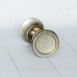 Può includere: Una maniglia per porta argentata con un designo decorativo a forma di corda attorno al bordo.