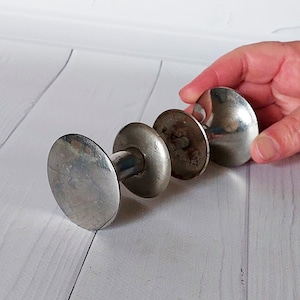 Może przedstawiać: Zestaw trzech starych, srebrnych gałek do drzwi. Gałki mają zaokrąglony, owalny kształt i są połączone metalowym prętem. Gałki wykazują oznaki zużycia i wieku, z pewnym matowieniem i przebarwieniami. Gałki są trzymane przez dłoń.
