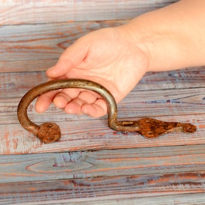 Könnte beinhalten: Ein rostiger Metallgriff mit einem gebogenen oberen Ende und einem flachen, spitzen unteren Ende. Der Griff ist aus Eisen und hat ein rustikales, gealtertes Aussehen.