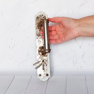 May include: A vintage, silver-toned door handle with a rusty finish. The handle is attached to a white metal plate with a keyhole.