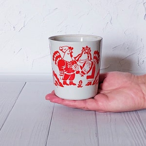 May include: White ceramic mug with a red rooster and hen design. The rooster is wearing a red and white patterned shirt and the hen is wearing a red and white patterned dress.