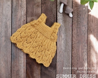 May include: A knitted yellow summer dress with a scalloped hem. The dress is laid out on a wooden surface with two crocheted mushrooms.