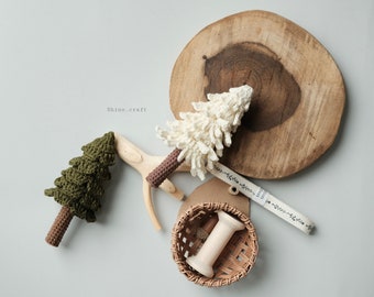 May include: Two crocheted Christmas trees, one green and one white, with brown wooden bases. The trees are on a wooden surface with a spool of white yarn in a wicker basket.