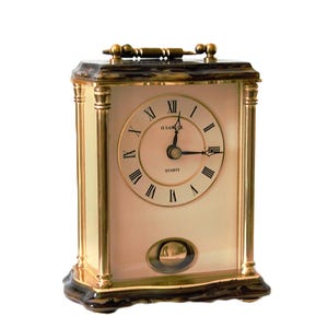 May include: A rectangular, gold-toned mantel clock with a cream-coloured face and Roman numeral hour markers. The clock has a pendulum and a handle on top. The clock face reads "H.RAMS" and "QUARTZ".