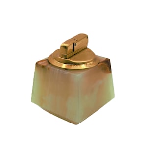 May include: A vintage lighter with a gold-toned metal top and a square base made of a translucent, marbled stone. The lighter's design is classic and elegant, with a focus on the contrast between the metal and stone.