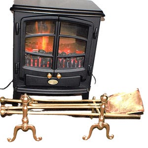 May include: A black electric stove featuring a simulated flame effect and glowing embers behind glass doors, accompanied by a set of brass fireplace tools including a shovel, poker, and tongs resting on a brass stand with curved legs.