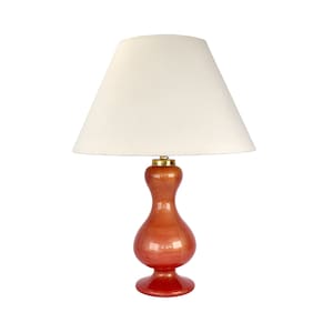 Puede incluir: Una lámpara de mesa de cerámica roja y naranja con una pantalla blanca en forma de tambor. La lámpara tiene una base en forma de calabaza.