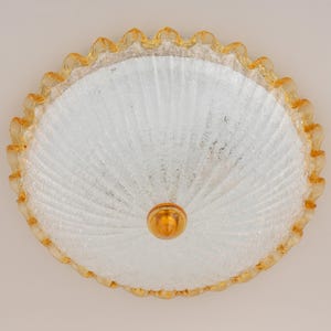 May include: A circular flush mount ceiling light fixture featuring a clear, ribbed glass dome with a textured finish. The outer edge is finished with a ruffled, amber-colored glass border, and a small, smooth, amber-colored glass finial sits at the center.