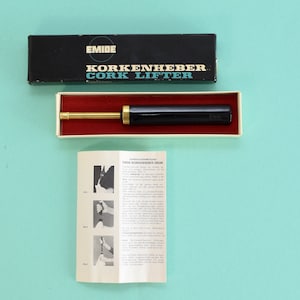 May include: A black and gold cork lifter in its original box with instructions. The box has the text "EMIDE KORKENHEBER CORK LIFTER" printed on it.