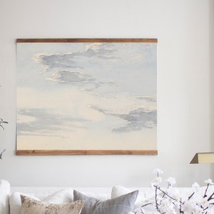 May include: A framed watercolour painting of a cloudy sky in shades of blue and white. The painting is hanging on a white wall in a living room setting.