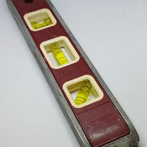 May include: A red and silver spirit level with three yellow bubble vials. The level is labelled "D. JOHNSON".
