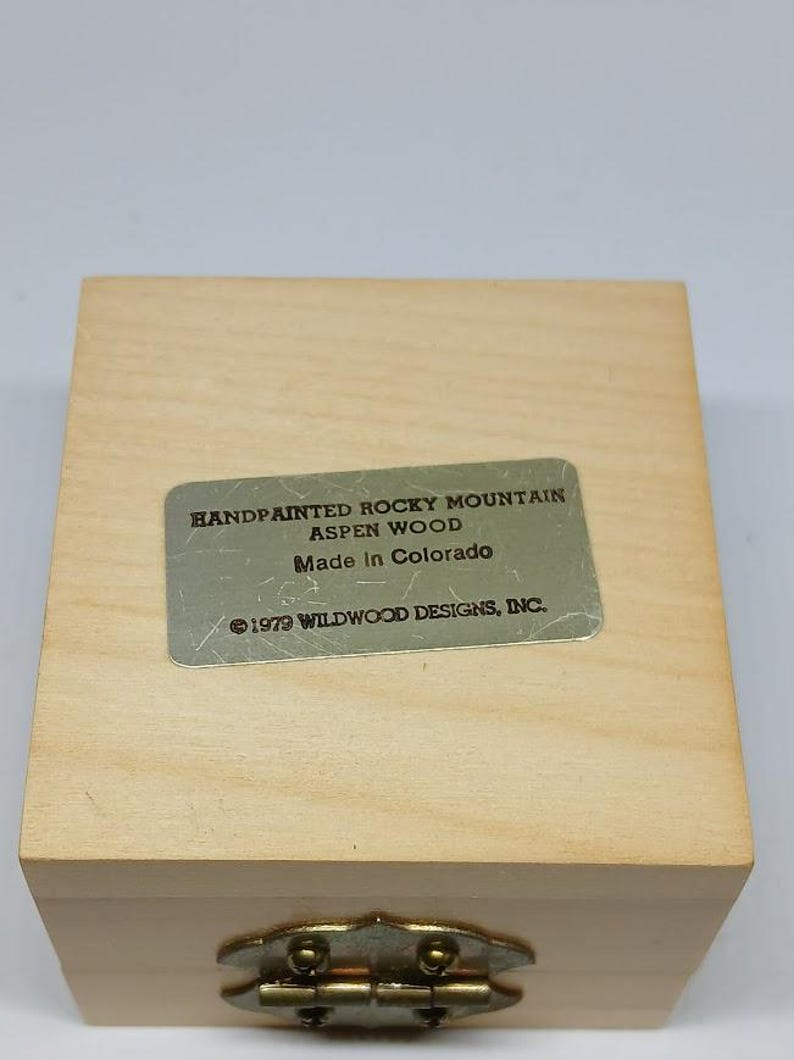 May include: A wooden box with a brass latch. The box has a label that reads "Handpainted Rocky Mountain Aspen Wood Made in Colorado &copy;1979 Wildwood Designs, Inc."
