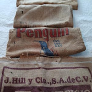 May include: Four hessian sacks, each showing varying degrees of wear. One sack displays the word "Penguin" in red lettering with a blue penguin illustration. The bottom sack has text reading "J. Hill y Cla., S.A. de C.V." and "BENEFICIO."