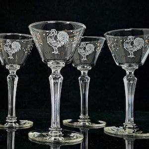 May include: A white ceramic mug with a black handle and the text "But First, Coffee" in a bold, black font. The mug is set against a blurred background, suggesting a cozy setting.