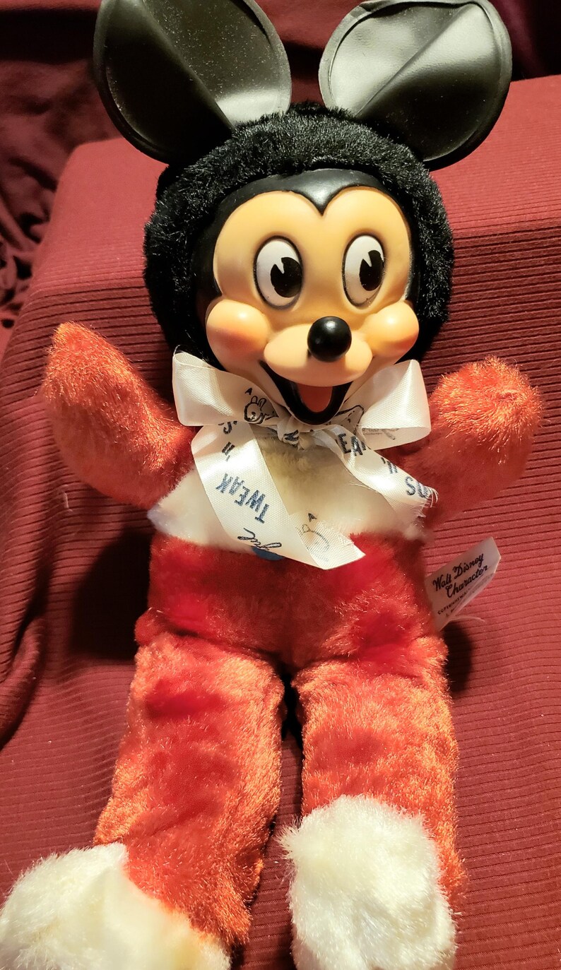May include: A vintage Mickey Mouse plush toy with a black head and ears, a red body, and white accents. The toy has a white ribbon around its neck with the word "Tweak" printed on it. A "Walt Disney Character" tag is attached.