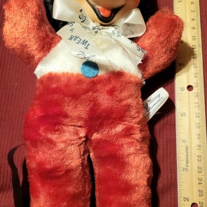 May include: Vintage Mickey Mouse plush doll with a black head, orange cheeks, and red plush body. The doll has a white collar with the text "Tweak" and a blue button. A tag reads "Walt Disney Character".