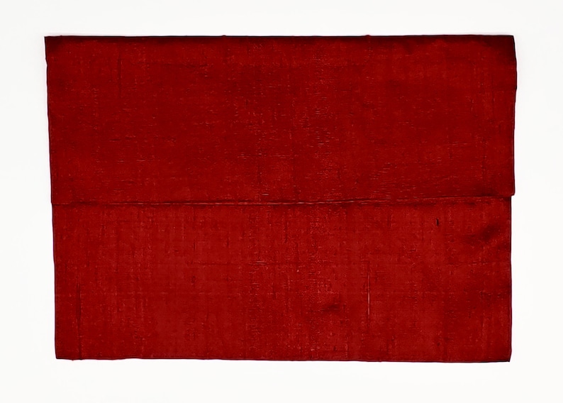 May include: A rectangular clutch bag in a deep, rich red color. The surface of the bag features a visible, fine-textured weave pattern throughout the fabric, creating a subtle grid-like appearance across the entire exterior of the accessory.