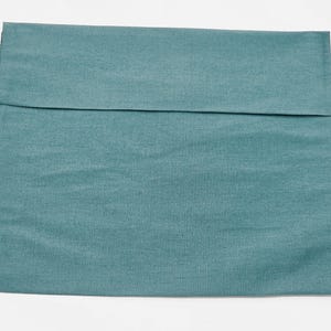 May include: A square pillow cover in a solid teal blue color with a visible horizontal seam across the upper portion. The fabric has a subtle woven texture and a matte finish, presenting a clean and simple design for a standard throw pillow.