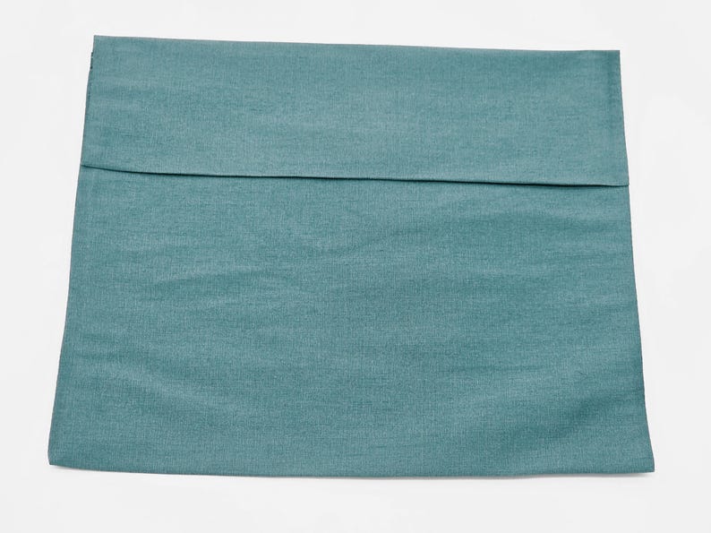 May include: A square pillow cover in a solid teal blue color with a visible horizontal seam across the upper portion. The fabric has a subtle woven texture and a matte finish, presenting a clean and simple design for a standard throw pillow.