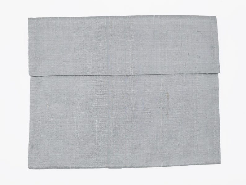 May include: A rectangular light gray fabric pouch with a visible woven texture. The item features a horizontal flap that folds over the main body, creating a clean, simple design with a consistent monochromatic color throughout the entire piece.