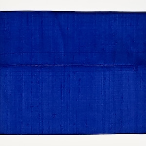 May include: A rectangular clutch bag in a vibrant royal blue color. The exterior features a textured, slubbed fabric surface with a horizontal seam running across the middle, creating a flap-like appearance with a clean, structured rectangular shape.
