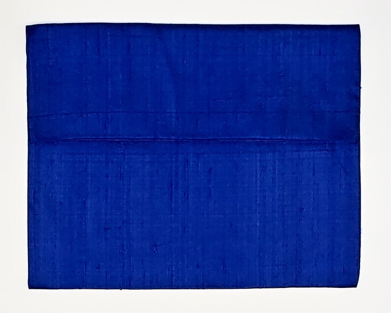 May include: A rectangular clutch bag in a vibrant royal blue color. The exterior features a textured, slubbed fabric surface with a horizontal seam running across the middle, creating a flap-like appearance with a clean, structured rectangular shape.