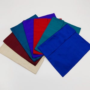 May include: A collection of rectangular fabric swatches arranged in a fan shape, featuring a variety of solid colors including cream, maroon, teal, purple, red, dark green, and bright blue, all displaying a subtle, smooth, and lustrous sheen.