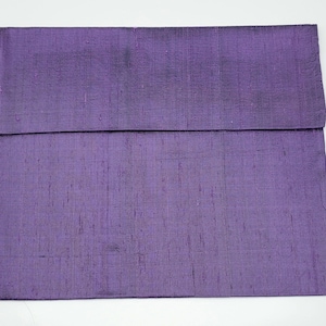 May include: A rectangular purple pillow cover featuring a visible slubbed texture throughout the fabric. The cover has a horizontal fold line across the upper section, creating a flap-like appearance with a consistent deep violet color tone.
