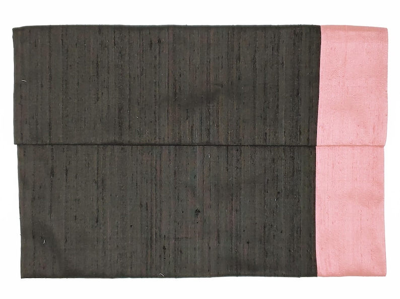 May include: A rectangular clutch bag featuring a dark charcoal gray main body with a visible slubbed texture and a contrasting solid light pink vertical panel on the right side. The design is simple and flat with a horizontal fold line across the center.