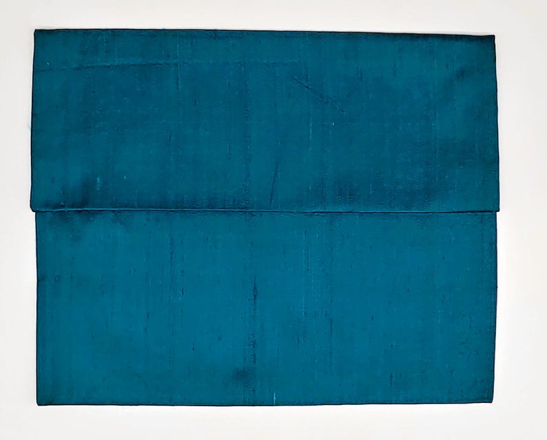 May include: A rectangular teal clutch bag with a smooth, slightly iridescent fabric finish. The bag features a horizontal flap closure that extends across the width of the item, creating a clean, structured silhouette with a consistent deep blue-green color.