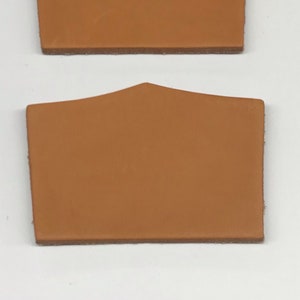 May include: Two brown leather patches with a pointed top and rounded edges. The patches are about 4 inches wide and 3 inches tall.