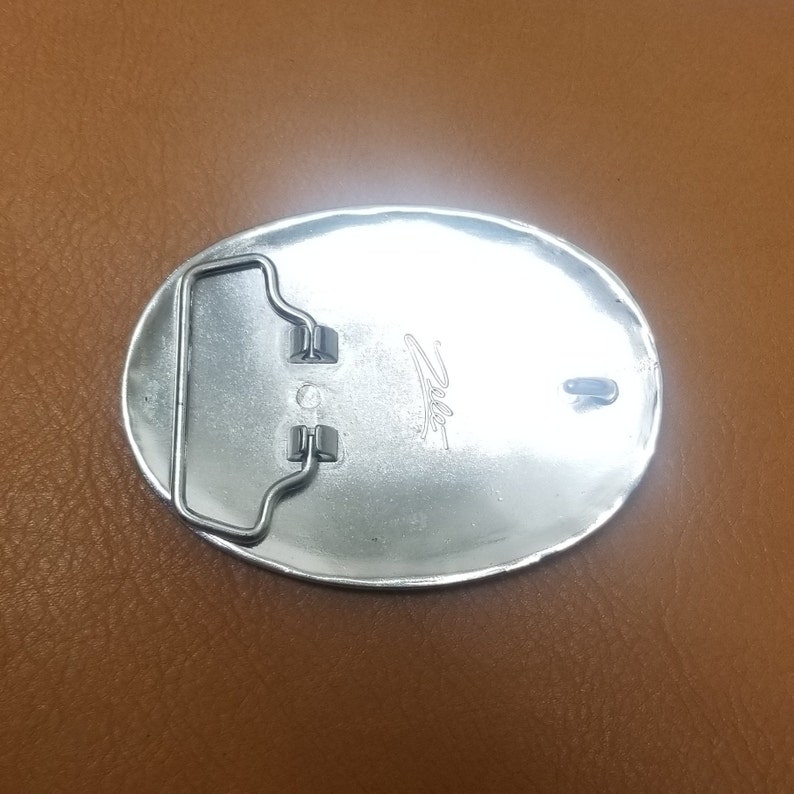 Puede incluir: Hebilla de cintur&oacute;n ovalada de plata con un bucle de metal y la palabra "Zito" grabada en la parte posterior.