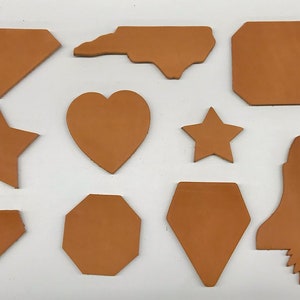 May include: A set of 10 leather shapes in various designs, including a heart, star, diamond, and rocket. The shapes are all a light brown color and are arranged on a white background.