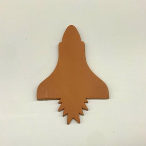 May include: A brown leather craft piece shaped like a rocket with a pointed top and a jagged bottom edge.