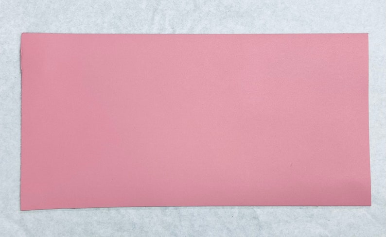 May include: A solid pink sheet of faux leather. The leather is smooth and has a subtle texture.