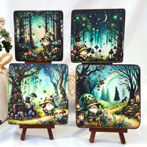 May include: Four square decorative art pieces featuring whimsical forest scenes with gnomes, mushrooms, and trees. Each piece is displayed on a small wooden easel. A vase with flowers and pinecones is in the background.