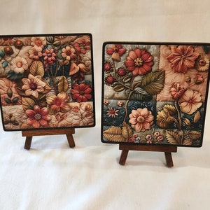 May include: Two small framed floral paintings on wooden easels. The paintings feature a patchwork design with colorful flowers and leaves.