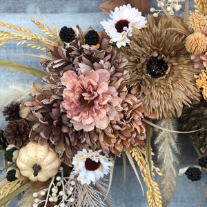 May include: A seasonal wreath with dried flowers, pinecones, and berries in autumnal tones of brown, beige, and cream. A small, cream-coloured pumpkin is also included. Ideal for decorating a home during the autumn season.