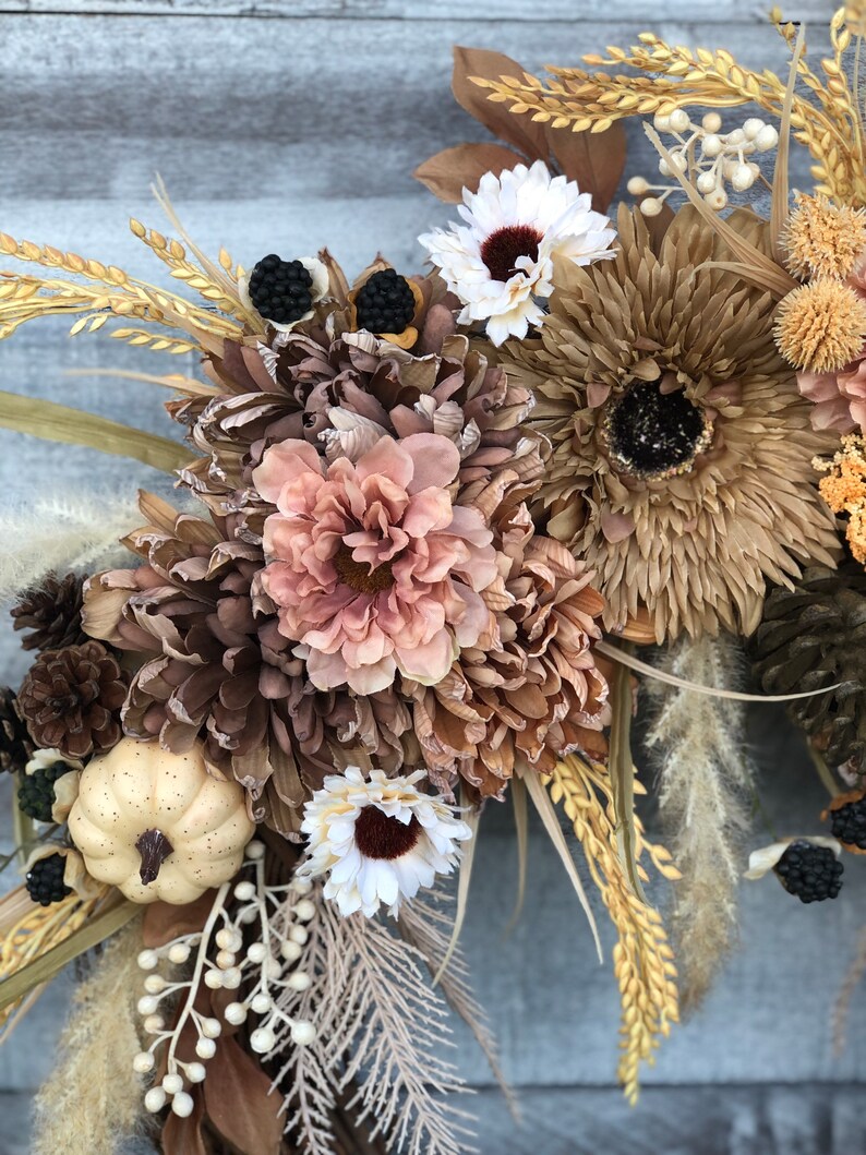 May include: A seasonal wreath with dried flowers, pinecones, and berries in autumnal tones of brown, beige, and cream. A small, cream-coloured pumpkin is also included. Ideal for decorating a home during the autumn season.